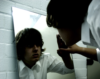 Young man searchingly looking at his reflection in a mirror